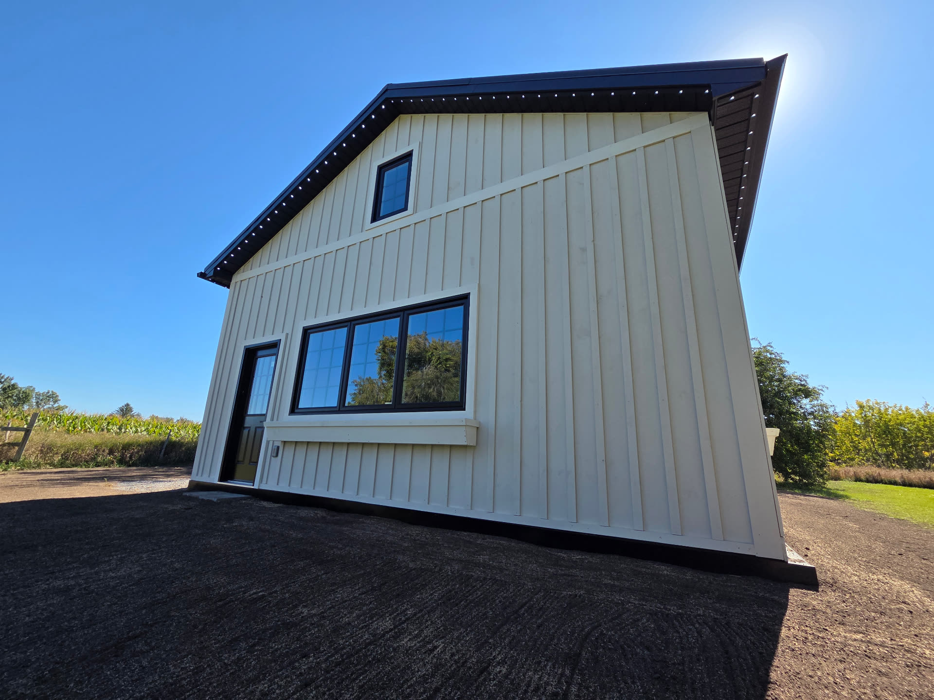 Cream barn with black trim at Warm Wishes install, permanent LED track visible along both rooflines in daylight
