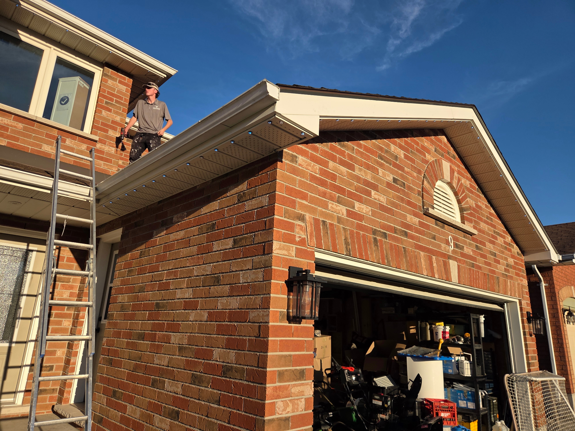 Warm Wishes installer securing permanent LED track along the eaves of a brick Belleville home