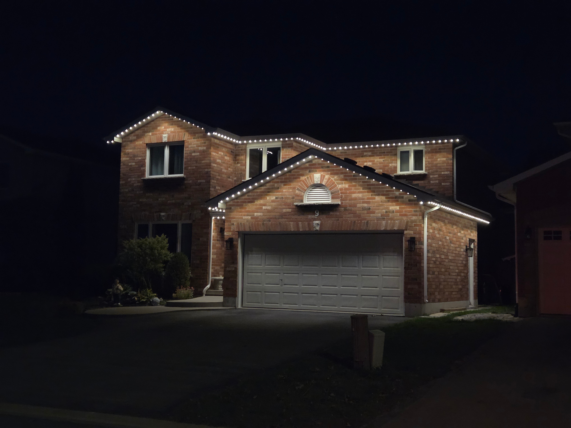 Belleville brick home at night with warm white permanent LED lights along every roofline